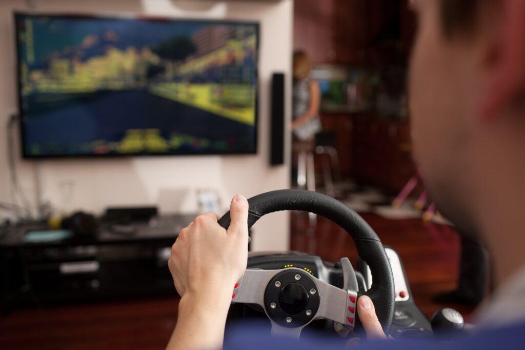 Man playing racing game with steering wheel simulator